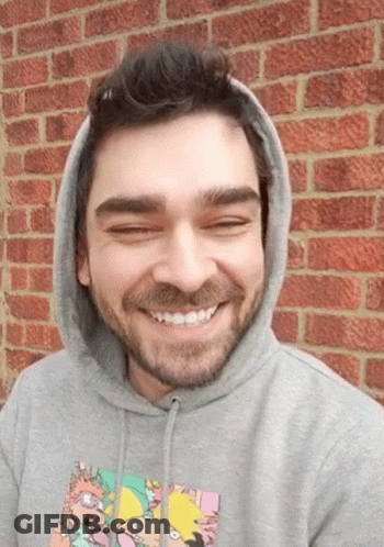 A Man Wearing A Rugrats Hoodie Smiles In Front Of A Red Brick Wall GIF