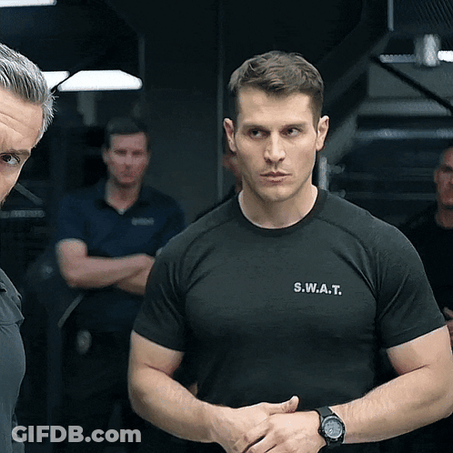 A Man Wearing A S.w.a.t. T-Shirt Stands In Front Of Another Man GIF