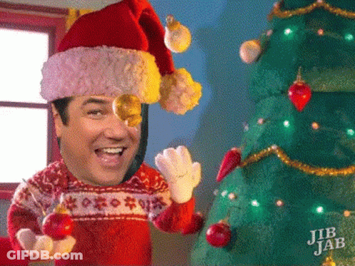 A Man Wearing A Santa Hat And Sweater Is Holding A Christmas Ball In Front Of A Christmas Tree GIF