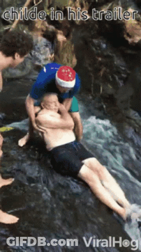 A Man Wearing A Santa Hat Is Helping Another Man In A Waterfall GIF