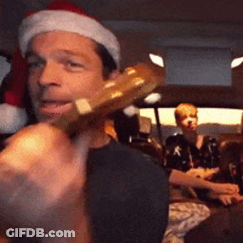 A Man Wearing A Santa Hat Is Holding A Guitar In His Hand GIF