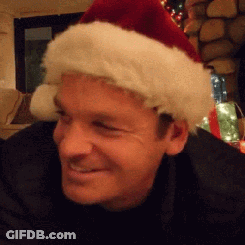 A Man Wearing A Santa Hat Is Smiling In A Living Room . GIF