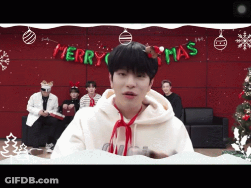 A Man Wearing A Santa Hat Stands In Front Of A Merry Christmas Banner GIF