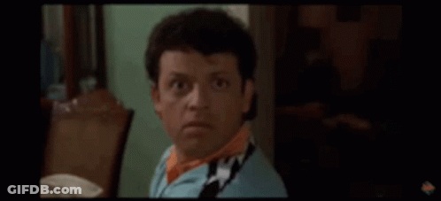 A Man Wearing A Scarf And A Blue Shirt Is Making A Funny Face . GIF