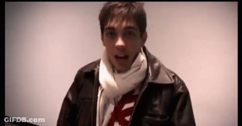 A Man Wearing A Scarf And A Leather Jacket Is Looking At The Camera GIF