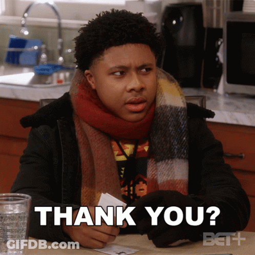 A Man Wearing A Scarf Is Sitting At A Table Holding A Piece Of Paper That Says Thank You GIF