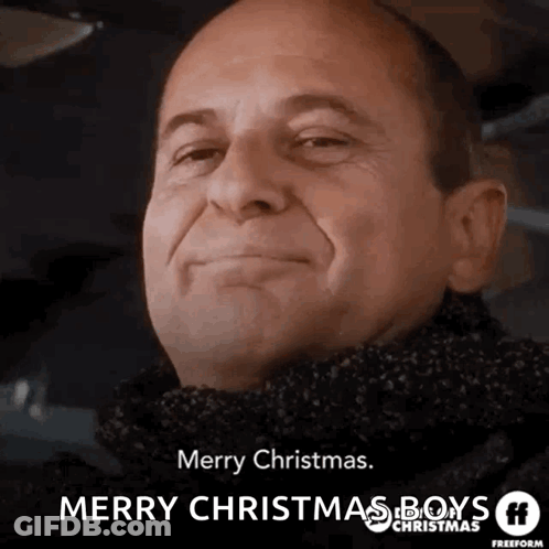 A Man Wearing A Scarf Is Smiling And Wishing Merry Christmas GIF