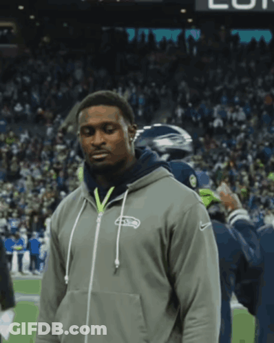 A Man Wearing A Seahawks Hoodie Stands On A Field GIF