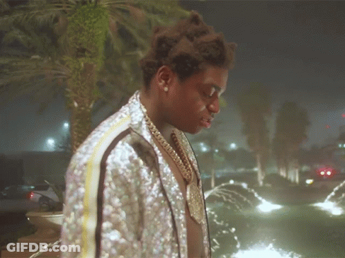A Man Wearing A Sequined Jacket Stands In Front Of A Fountain GIF