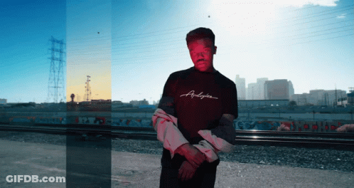 A Man Wearing A Shirt That Says Andyson Stands In Front Of A City GIF