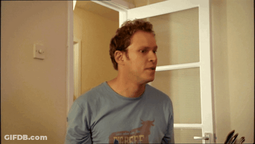 A Man Wearing A Shirt That Says Dig Here Is Standing In Front Of A Door GIF