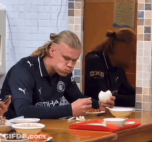 A Man Wearing A Shirt That Says Etihad Is Eating Food GIF