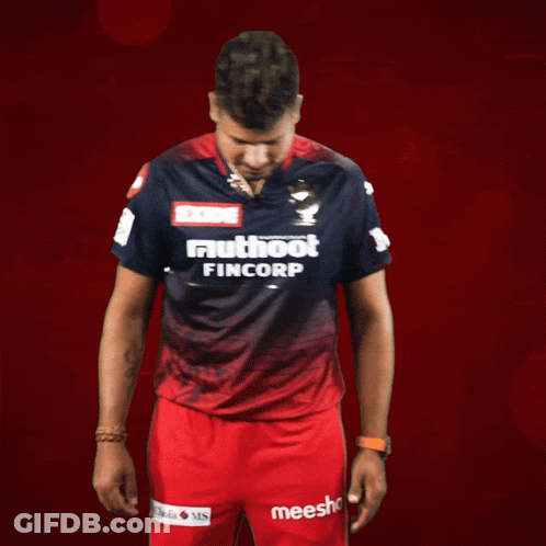 A Man Wearing A Shirt That Says Exide Muthoot Fincorp Stands In Front Of A Red Background GIF