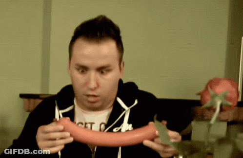 A Man Wearing A Shirt That Says Get On Holds A Sausage GIF