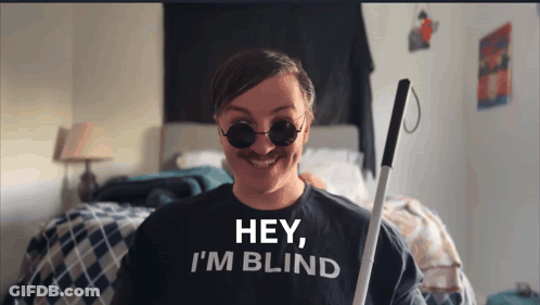 A Man Wearing A Shirt That Says Hey I 'M Blind Is Holding A Cane GIF