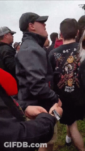 A Man Wearing A Shirt That Says Hot Rod Is Standing In A Crowd Of People GIF