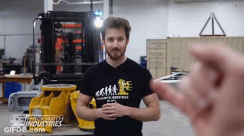 A Man Wearing A Shirt That Says Jacksmith Industries Stands In A Factory GIF