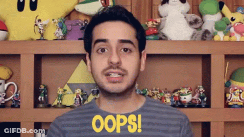 A Man Wearing A Shirt That Says Oops Is Standing In Front Of A Shelf Full Of Toys GIF