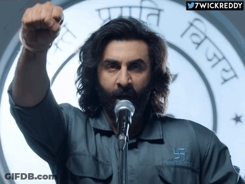 A Man Wearing A Shirt That Says Swastik Trust GIF