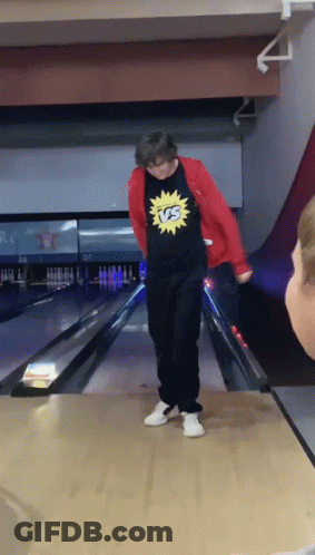 A Man Wearing A Shirt That Says Vs On It Stands On A Bowling Alley GIF