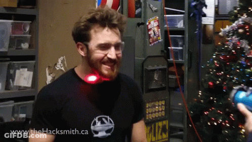 A Man Wearing A Shirt That Says Www.thehacksmith.ca Smiles In Front Of A Christmas Tree GIF