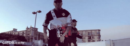 A Man Wearing A Shirt That Says Xxx On It Stands Next To Another Man GIF