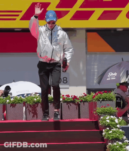 A Man Wearing A Silver Jacket And A Blue Hat Stands On A Stage In Front Of Dhl GIF