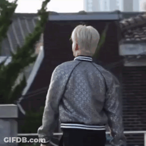 A Man Wearing A Silver Jacket Is Standing In Front Of A Building GIF