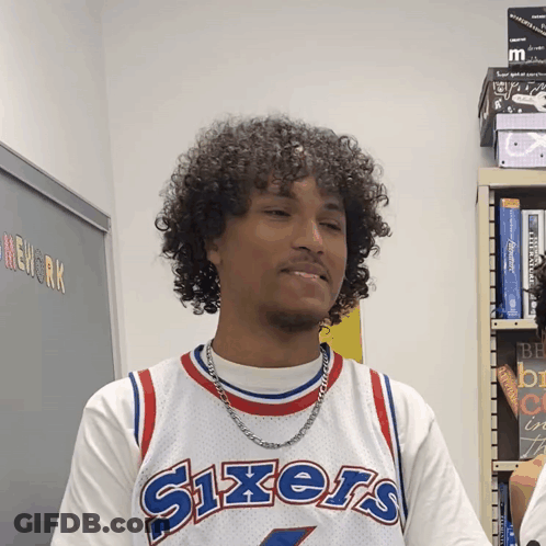 A Man Wearing A Sixers Jersey Stands In Front Of A Blackboard GIF