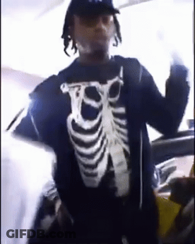A Man Wearing A Skeleton Shirt Is Standing In Front Of A Car And Giving The Middle Finger . GIF