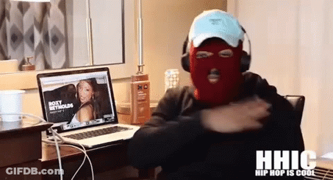 A Man Wearing A Ski Mask Is Sitting In Front Of A Laptop With A Picture Of Roxy Metcalfe On The Screen GIF