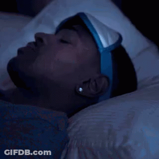 A Man Wearing A Sleep Mask Is Laying In Bed At Night . GIF