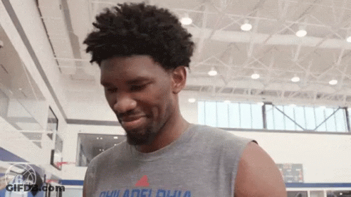 A Man Wearing A Sleeveless T-Shirt That Says Philadelphia Is Standing In A Gym . GIF