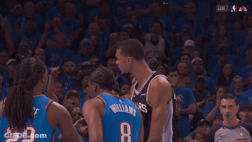 A Man Wearing A Spurs Jersey Stands In Front Of A Crowd GIF