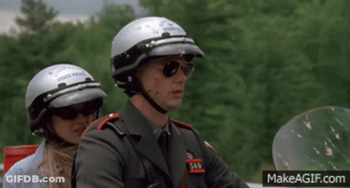 A Man Wearing A State Police Helmet Sits Next To A Woman Wearing Sunglasses GIF