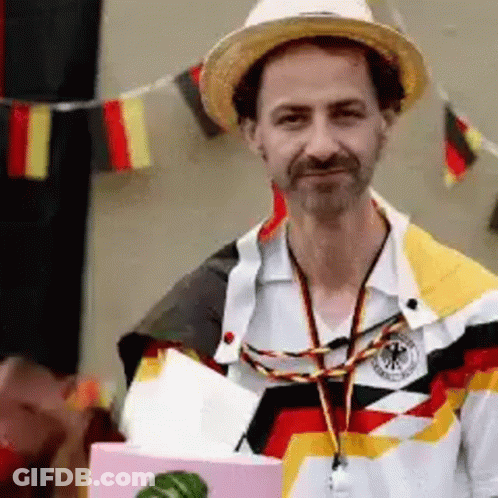 A Man Wearing A Straw Hat And A German Shirt Is Holding A Box GIF