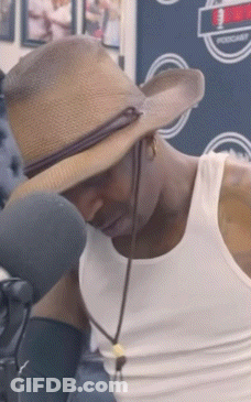 A Man Wearing A Straw Hat And A White Tank Top Looks Down GIF