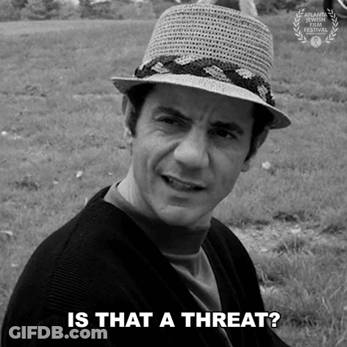 A Man Wearing A Straw Hat Says " Is That A Threat " In A Black And White Photo GIF