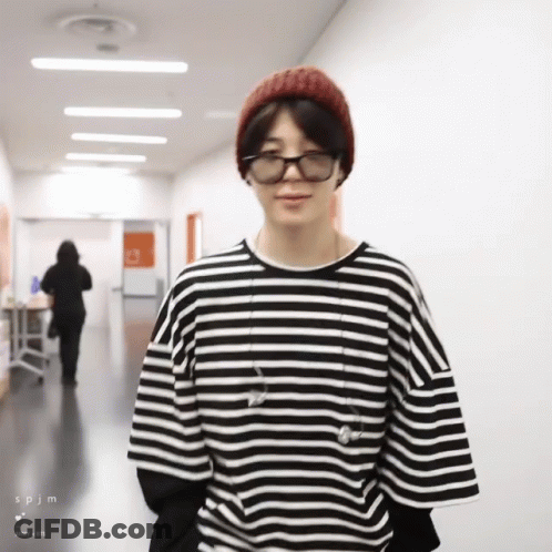 A Man Wearing A Striped Shirt And A Beanie Is Standing In A Hallway GIF