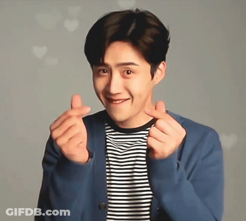 A Man Wearing A Striped Shirt And A Blue Jacket Is Making A Heart With His Hands GIF