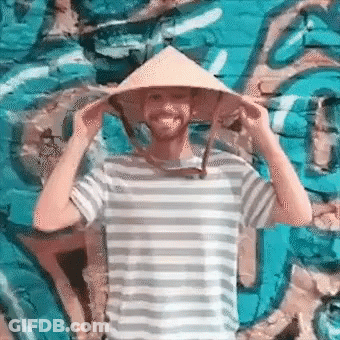 A Man Wearing A Striped Shirt And A Conical Hat Is Standing In Front Of A Blue Wall . GIF