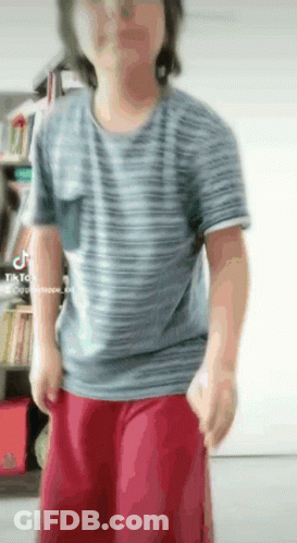 A Man Wearing A Striped Shirt And Red Shorts Is Standing In A Room . GIF