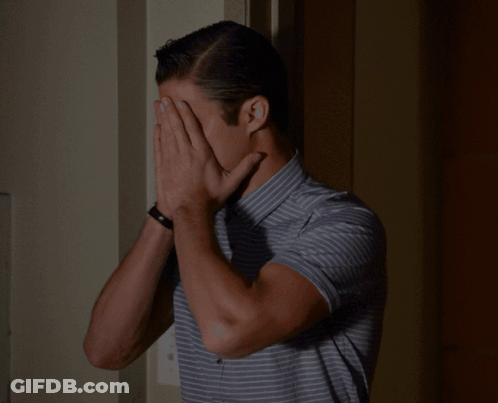 A Man Wearing A Striped Shirt Is Covering His Nose With His Hand GIF