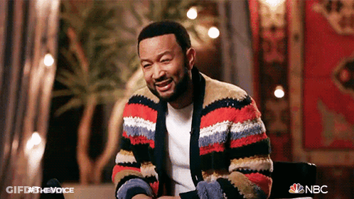 A Man Wearing A Striped Sweater Is Sitting In A Chair And Smiling GIF