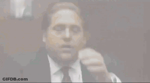 A Man Wearing A Suit And Tie Is Covering His Face With His Hand . GIF