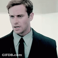 A Man Wearing A Suit And Tie Is Looking At The Camera . GIF