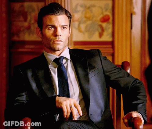 A Man Wearing A Suit And Tie Is Sitting In A Chair . GIF