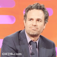 A Man Wearing A Suit And Tie Is Sitting In Front Of An Orange Background . GIF