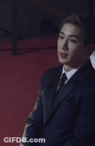 A Man Wearing A Suit And Tie Is Sitting On A Red Carpet . GIF
