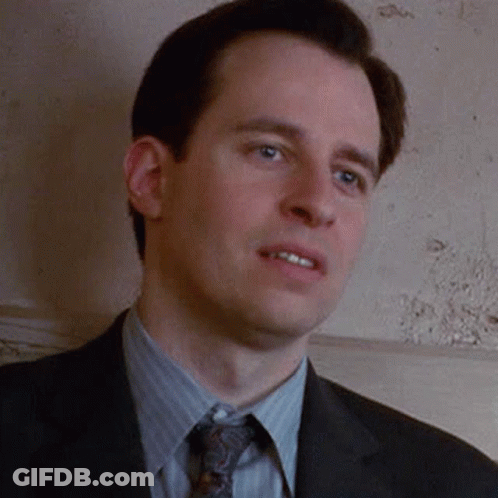A Man Wearing A Suit And Tie Is Standing In Front Of A Wall . GIF